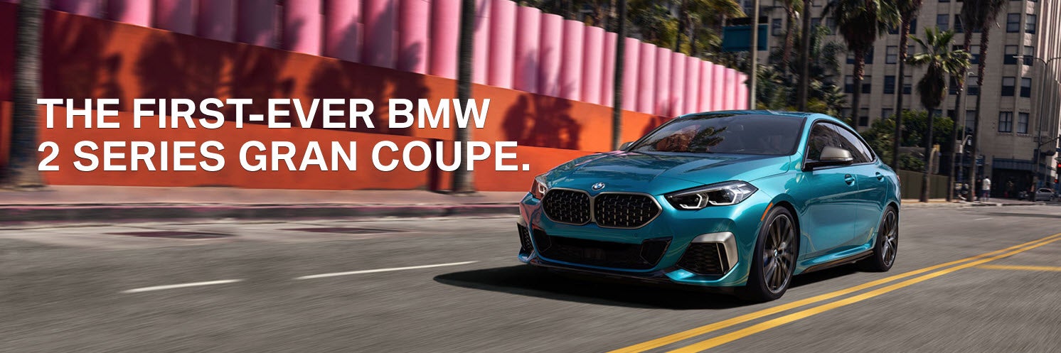 A blue metallic BMW 2 Series Gran Coupe driving down street during the day.