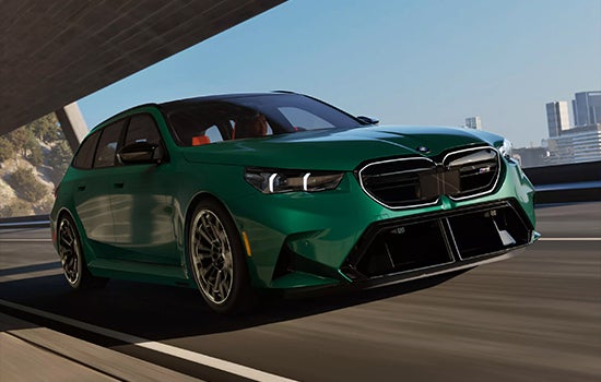 Green BMW M5 Touring driving on a city road. | Open Road BMW of Edison in Edison NJ