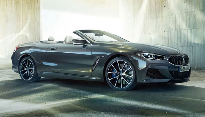 A blue metallic BMW 8 Series Convertible parked by concrete pillars.