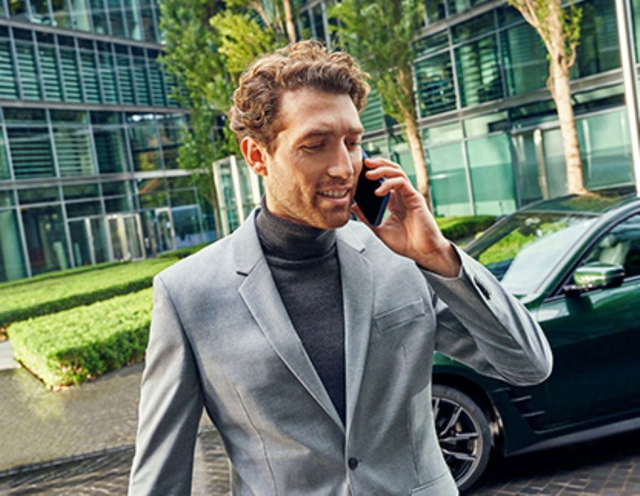 A man speaks on a phone with a BMW parked in the background